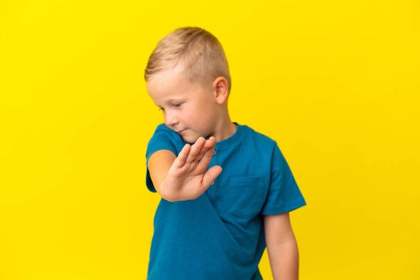 Маленький русский мальчик изолирован на желтом фоне, делая остановку жест и разочарование - Фото, изображение