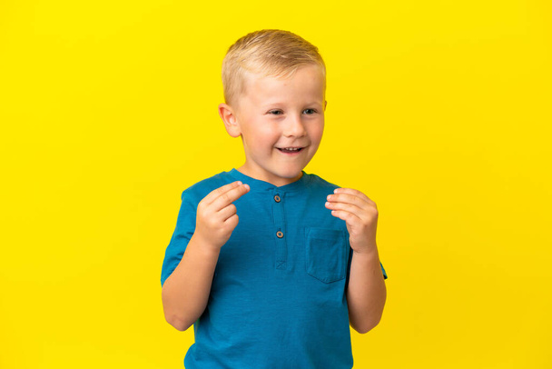 Little Russian boy isolated on yellow background making money gesture - Photo, Image