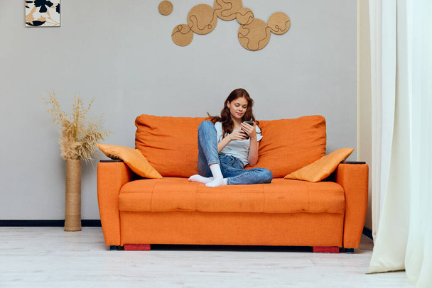 retrato de una mujer con el pelo largo está sentado en el sofá con un teléfono inalterado - Foto, Imagen