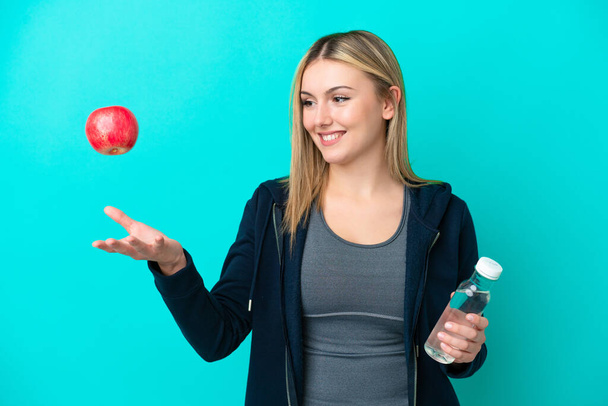 Jonge blanke vrouw geïsoleerd op blauwe achtergrond met een appel en met een fles water - Foto, afbeelding