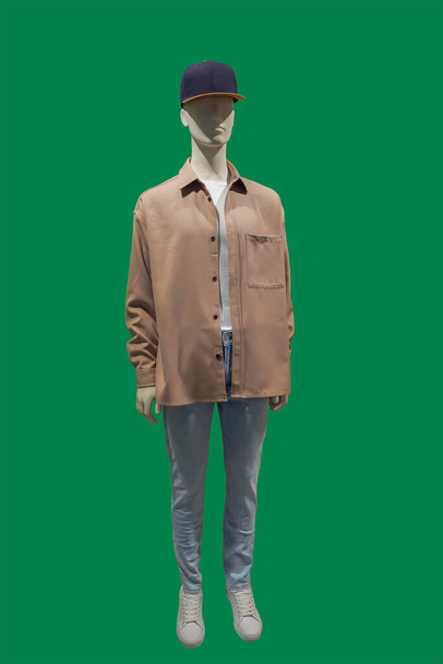 Full length image of a male display mannequin wearing brown jacket and blue jeans isolated on a green background - Fotoğraf, Görsel