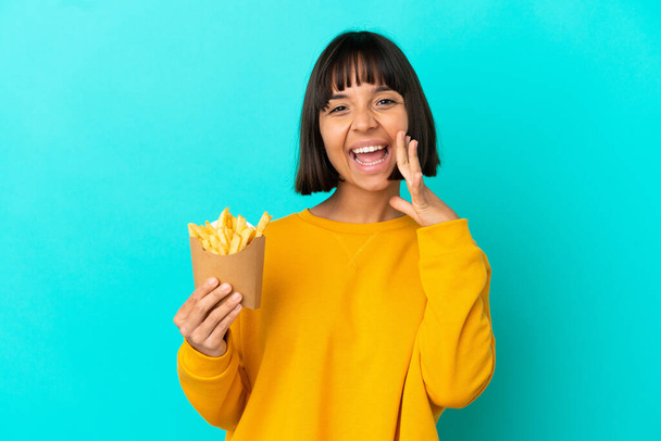 Jeune femme brune tenant des frites sur fond bleu isolé criant avec la bouche grande ouverte - Photo, image