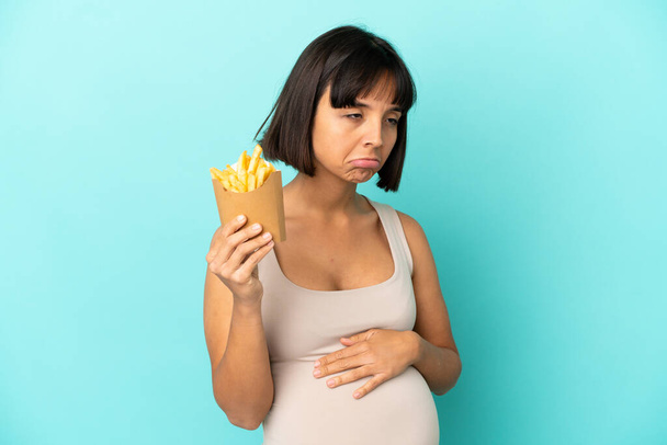 Молода вагітна жінка тримає смажені чіпси над ізольованим синім тлом
 - Фото, зображення