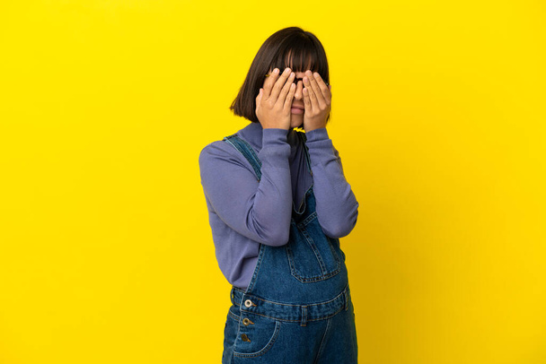 Young pregnant woman over isolated yellow background covering eyes by hands - Foto, afbeelding