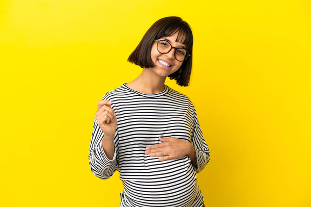 Young pregnant woman over isolated yellow background laughing - Valokuva, kuva