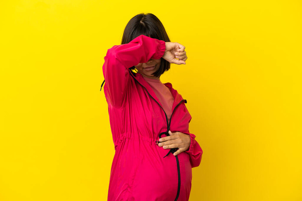Nuori raskaana oleva nainen yli eristetty keltainen tausta peittää silmät käsin - Valokuva, kuva