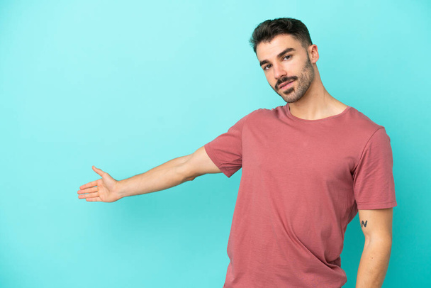 Young caucasian man isolated on blue background extending hands to the side for inviting to come - Foto, imagen