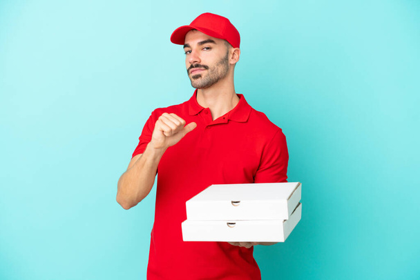 Livraison homme caucasien ramasser des boîtes de pizza isolé sur fond bleu fier et auto-satisfait - Photo, image
