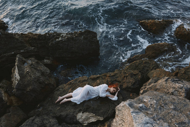 Barefoot woman in a white dress lying on a stone in a white dress view from above - Foto, Imagen