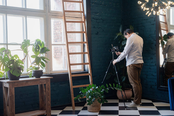 植物とスタイリッシュな青いリビングルームで働く男性写真家 - 写真・画像