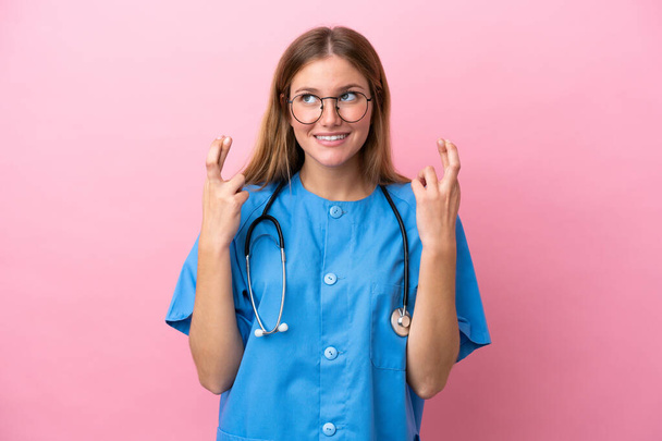 Jonge chirurg arts vrouw geïsoleerd op roze achtergrond met vingers kruisen - Foto, afbeelding