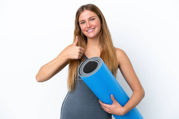 Young sport woman going to yoga classes while holding a mat giving a thumbs up gesture - Valokuva, kuva