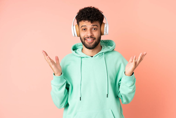 Nuori marokkolainen mies eristetty vaaleanpunainen tausta yllättynyt ja kuuntelee musiikkia - Valokuva, kuva