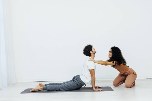 mujer enseña hombre haciendo gimnasia yoga asana en una habitación blanca - Foto, imagen