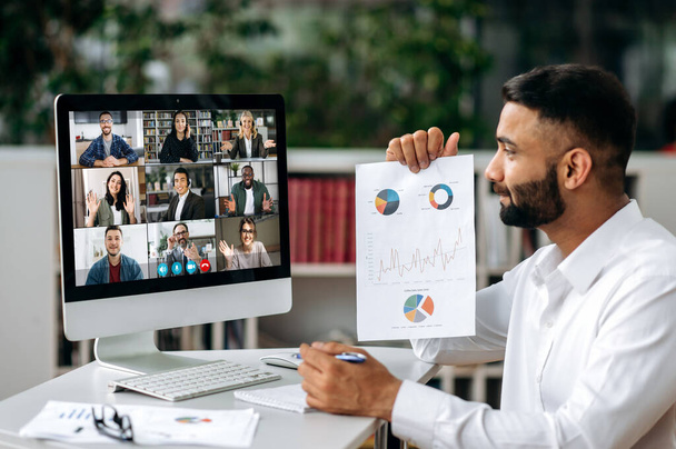 Video conference, online meeting. Intelligent Indian business man or mentor sits at workplace, communicates by video call with his partners, discuss a strategy, shows a financial graph - Photo, Image