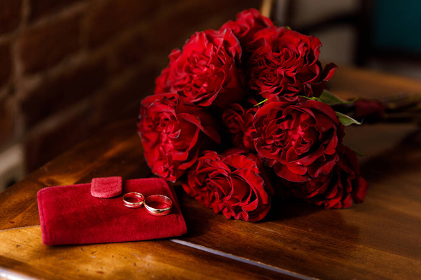 Dva snubní prsteny v bílém a červeném zlatě s svatební kyticí s červenými růžemi - Fotografie, Obrázek