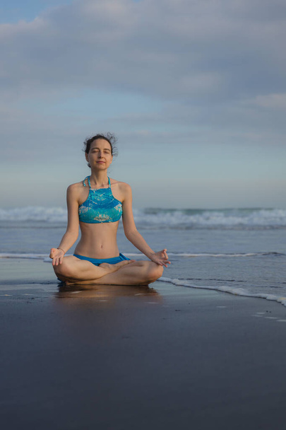 Yoga practice on the beach. Lotus pose. Padmasana. Hands in gyan mudra. Closed eyes. Meditation and concentration. Zen life. Relaxation of body and mind. Yoga retreat. Sunset time. Copy space. Bali - Fotó, kép