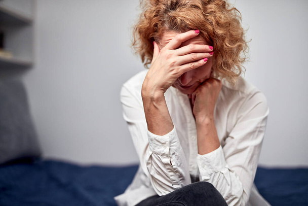 Femme avec des maux de tête, gueule de bois, problèmes mentaux et de dépression assis sur un lit à la maison. - Photo, image
