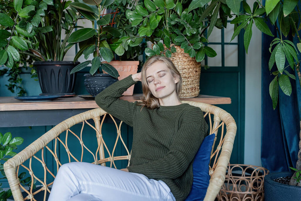 Volný čas. Mladá blondýna žena sedí v pohodlném křesle obklopen rostlinami - Fotografie, Obrázek