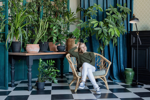 Leisure time. Young blonde woman sitting in comfortable chair surrounded with plants - Foto, Bild