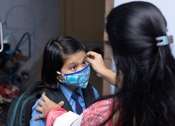 Una madre indiana prepara il suo bambino ragazza con protezione maschera naso da inviare a scuola dopo pandemia - Foto, immagini