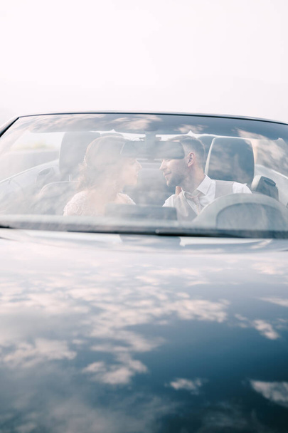 Bride and groom sit in the car and look at each other - Photo, image