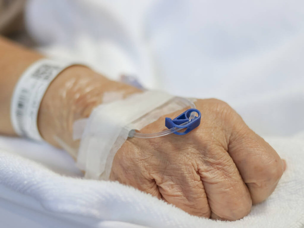 Nahaufnahme der Hand einer Seniorin mit Tropfen oder medizinischem Tropfen im Krankenhaus. Patientenhand mit Tropf. - Foto, Bild