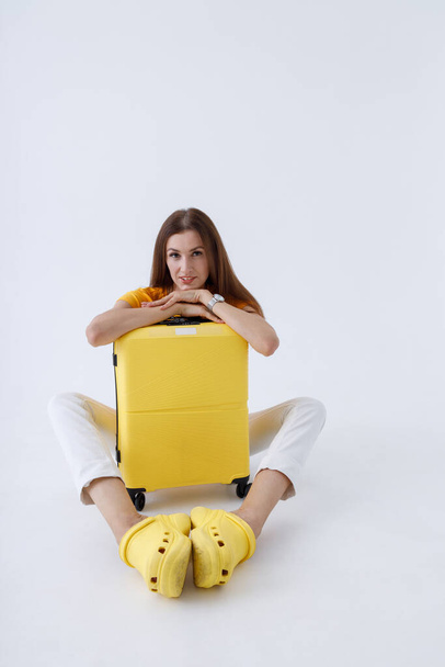 Γοητευτική γυναίκα κάθεται με ταξιδιωτική τσάντα ανάμεσα στα πόδια της - Φωτογραφία, εικόνα
