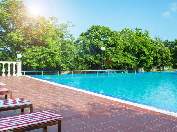Πολυτελής εξωτερική πισίνα με ξαπλώστρες, δέντρα στο παρασκήνιο, φως του ήλιου. - Φωτογραφία, εικόνα