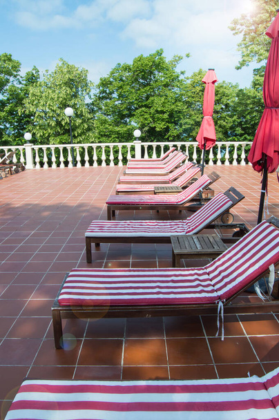 Άδειο ξύλινο κατάστρωμα καρέκλες με κόκκινο και λευκό ριγέ στρώματα σταθεί στη σειρά. Πολυτελής υπαίθρια αναψυχή, κάθετη φωτογραφία. - Φωτογραφία, εικόνα