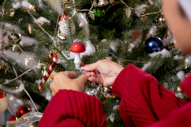 Feliz jovem asiático mulher sorrindo pendurado decoração ornamento na árvore de Natal na sala de estar em casa, ação de graças véspera dia e ano novo, celebração de férias, interior, uma pessoa. - Foto, Imagem