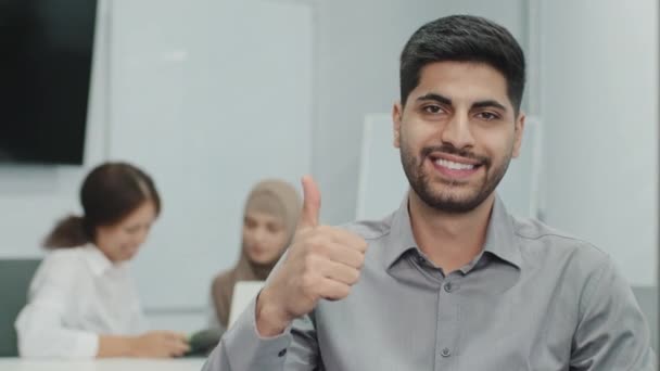Портрет счастливого улыбающегося арабского бизнесмена, делающего большой палец вверх, как жест перед камерой. Сотрудник доволен работой и работает с отличной командой. Клиент позитивно отзывается об услугах компании - Кадры, видео