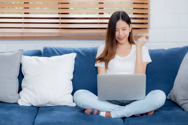 Junge asiatische Geschäftsfrau lächelt und arbeitet von zu Hause mit Laptop-Computer online zum Internet auf Sofa im Wohnzimmer, freiberufliche Mädchen mit Notizbuch auf Couch mit Komfort, neue normale, Lifestyle-Konzept. - Foto, Bild