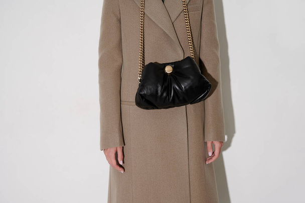 Woman in beige coat with black leather handbag on a golden chain. Flap bag on the white background. Horizontal photo. White background. - 写真・画像