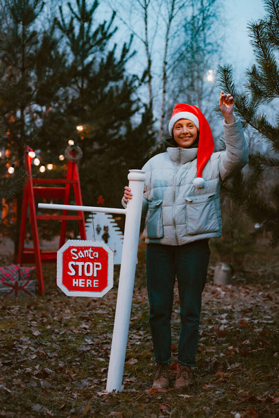 Hipster-Frau mit Nikolausmütze und Wunderkerze zündet hier ein Stoppschild mit dem Text Weihnachtsmann an. - Foto, Bild