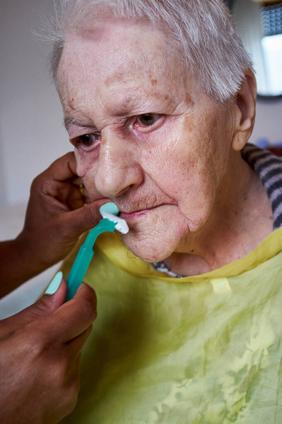 elderly woman receiving facial hair removal from african american caregive - Photo, Image