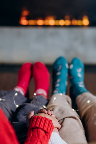 Couple holds hands sitting near fireplace in colorful socks - Foto, imagen