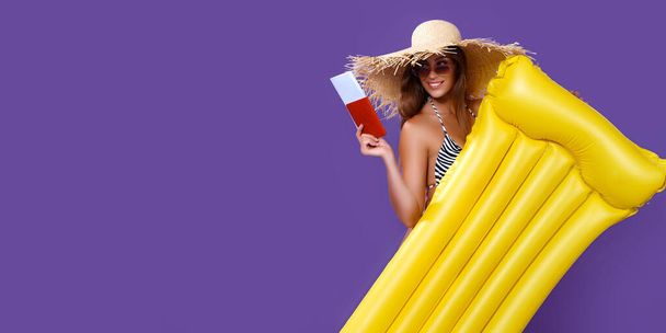 Smiling girl ready to summer vacations stands with yellow inflatable mattress holds ticket, passport - Fotó, kép