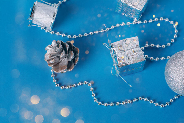 Silver baubles of Christmas decoration with golden lights on a blue background. Christmas balls, gift box, pine cones and new year's beads for the tree. Flat lay. - Φωτογραφία, εικόνα