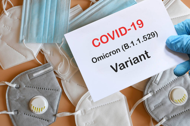 Doktorun elinde beyaz kağıtlı mavi eldiven ve arka planda çeşitli koruma maskeleri olan Covid-19 Omicron Variant mesajı var. COVID-19 omikron varyant türü koruma kavramı. - Fotoğraf, Görsel