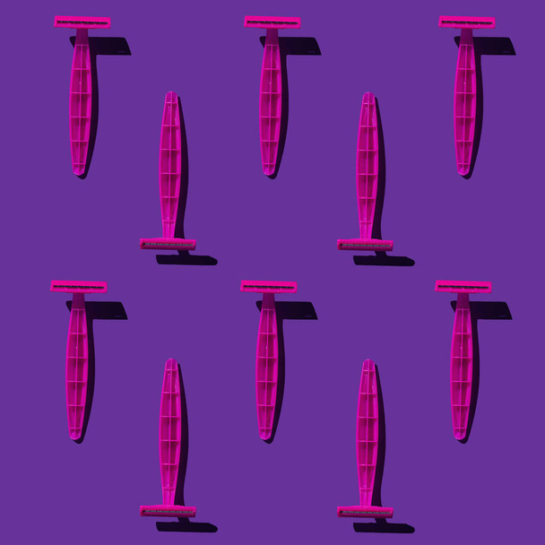 Eine Gruppe pinkfarbener Kunststoffrasierer. Nahtloses Muster. Leuchtend rosa Rasiermesser auf einem leuchtend violetten Hintergrund. Gedreht mit rauem Licht, harten schwarzen Schatten. - Foto, Bild