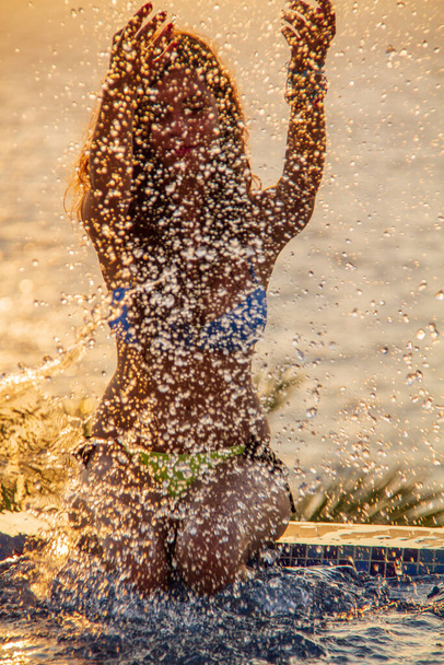 Une jeune femme joue à la piscine au bord de la mer éclaboussant l'eau à Pomos, Chypre - Photo, image
