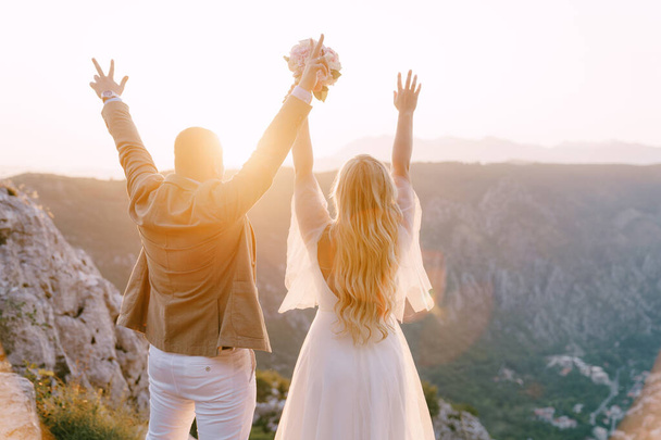 Groom and bride stand with raised hands on the background of mountains - Photo, Image