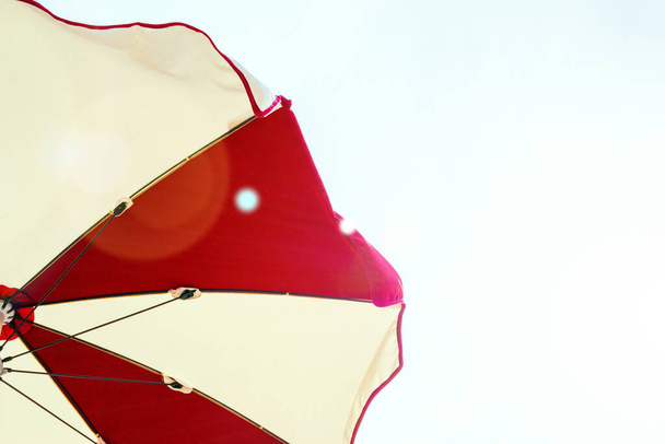 Зонтичный пляж. Красный летний пляжный зонтик на голубом морском фоне. Солнечный зонтик для отпуска. Отдых на открытом воздухе в океане с копировальным пространством - Фото, изображение