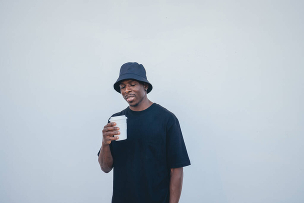 A young black man in street-style clothes holding his takeaway drink on a white background - Foto, immagini