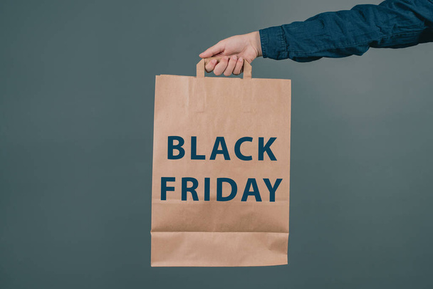 Young man is holding a shopping bag with the phrase black friday, dark colored background, big sale - Fotografie, Obrázek