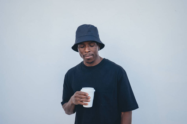 A young black man in street-style clothes holding his takeaway drink on a white background - Fotografie, Obrázek