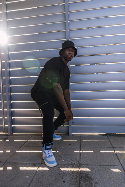 A vertical shot of a young black man from Spain in street-style black clothing and bright shoes - Fotoğraf, Görsel