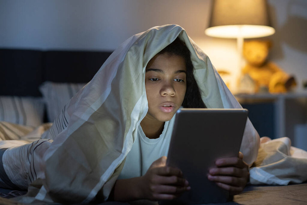Mädchen unter Bettdecke surft im Netz auf Tablet - Foto, Bild