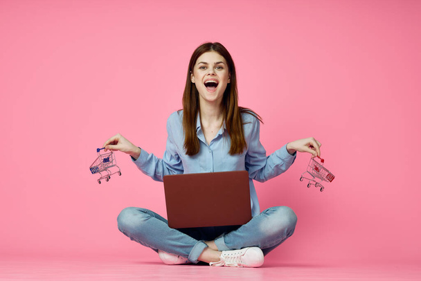 woman sitting on floor with laptop shopping entertainment pink background - Фото, изображение